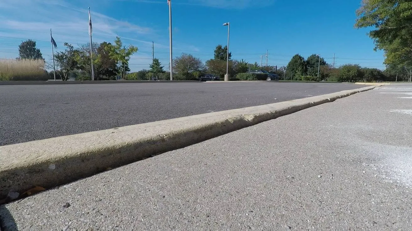 A concrete parking lot apron settled below the curb beside it, photographed at ground level.
