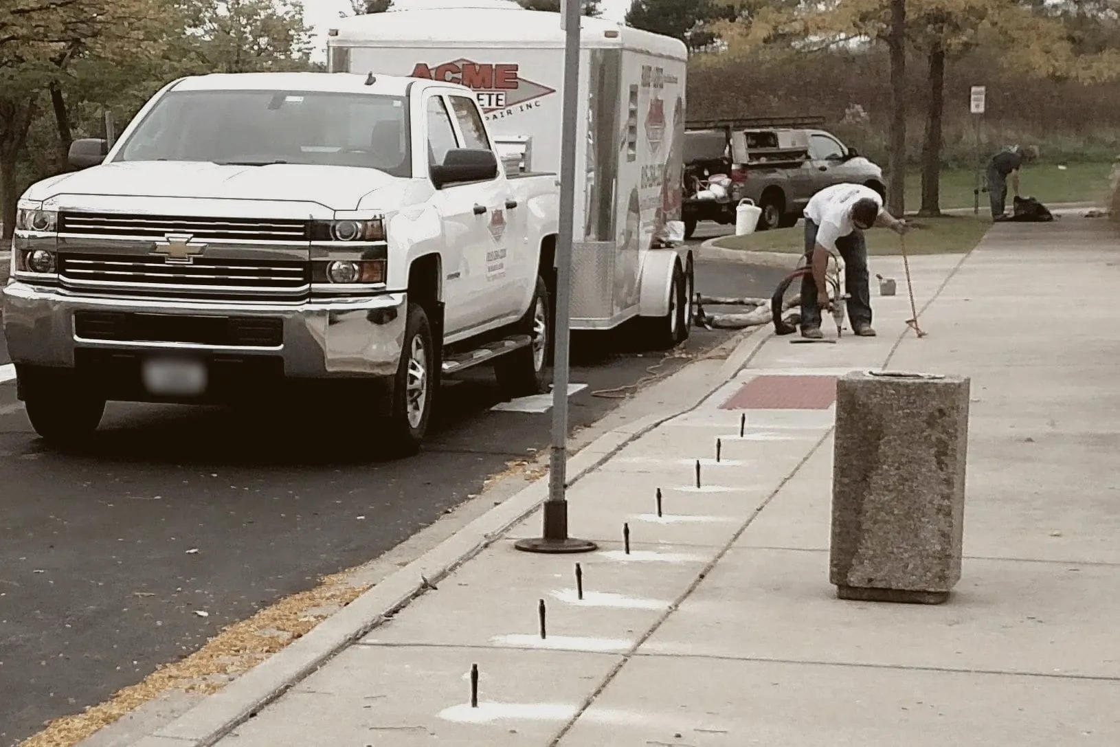 A row of ports down a municipal sidewalk while a crew member drills